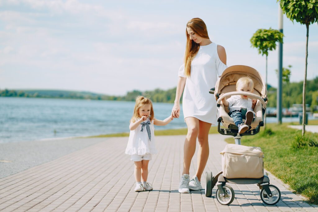 a beautiful young long-haired mom in the park with her beautiful little son and charming daughter with a mommy bag on kids trolly